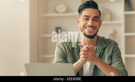 Man Smiles While Sitting at Desk With Laptop in Bright Room During the Day Stock Photo