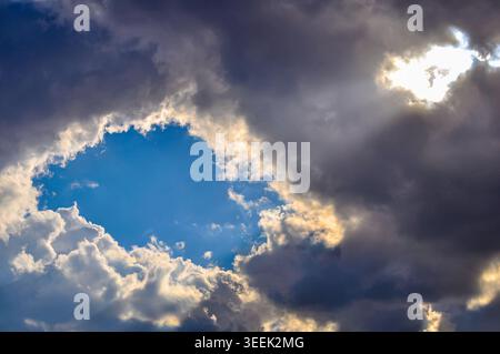 A dramatic low-angle landscape photo captures a powerful, intense azure blue void of sky framed by thick, dark, and light-edged cumulonimbus clouds. A Stock Photo