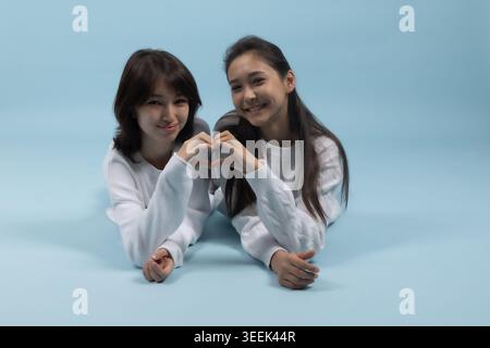 Two girls making heart shape - lying down and forming heart with hands Stock Photo