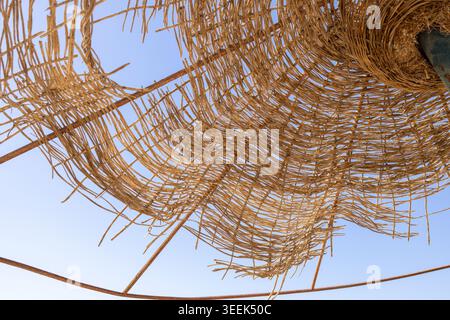 Close view of a woven straw beach umbrella against a pale blue sky creating an abstract tropical summer holiday composition with natural texture and r Stock Photo