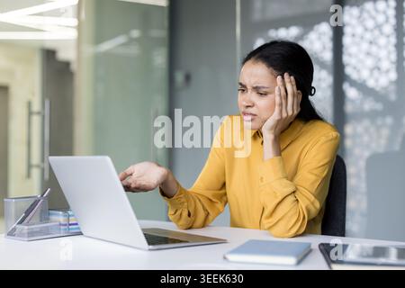 Stressed young businesswoman at her desk struggling with a malfunctioning laptop, looking frustrated and overwhelmed by software or connectivity errors while trying to meet a deadline Stock Photo