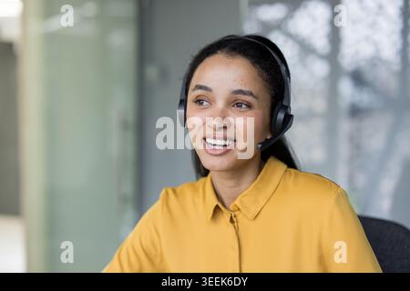 Smiling call center agent wearing a headset and talking with a client, providing excellent customer service and support while working in a modern office environment Stock Photo