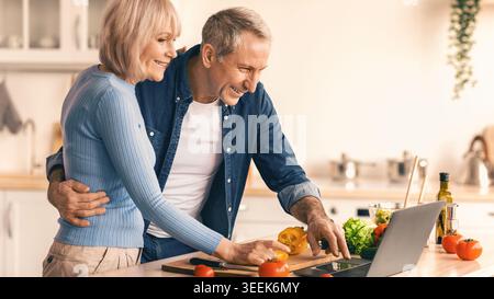 Couple Cooks Together in Kitchen Using Laptop for Recipe in Afternoon Stock Photo