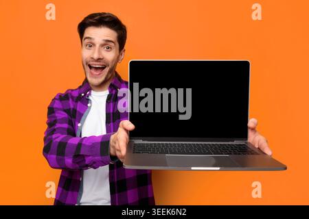 Man Holds Empty Laptop in Front of Orange Wall While Smiling and Looking at the Camera Stock Photo