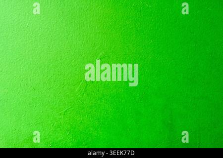 Full frame texture of a vibrant green painted wall with a subtle grainy surface and light gradient, abstract background Stock Photo