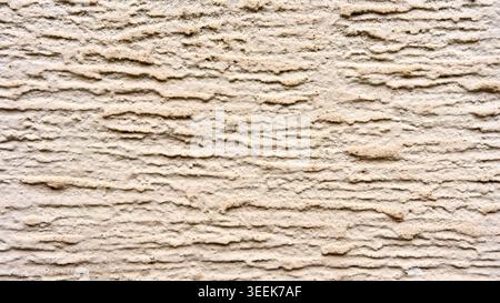 Close-up of a rough beige decorative plaster wall texture with horizontal relief ridges creating an abstract background. Stock Photo