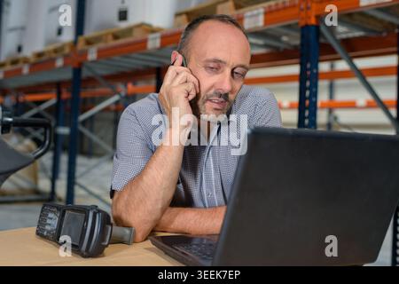 warehouse worker with laptop and scanner using smartphone Stock Photo
