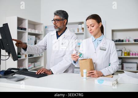 Middle aged Indian man and young woman pharmacists processing prescription order and checking inventory in pharmacy. For healthcare retail, medication service, team workflow Stock Photo