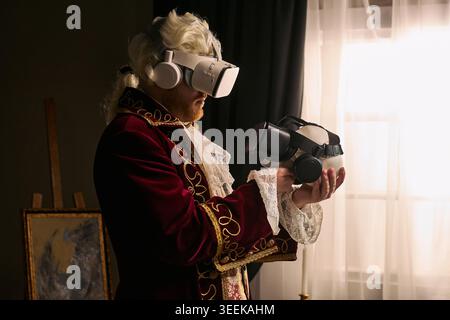 Man wearing historical costume and using virtual reality headset while holding second device, illustrating innovation contrast. For tech marketing or future concept campaigns Stock Photo