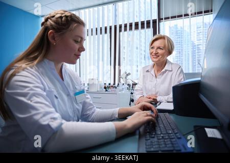 Young woman typing on computer with middle-aged woman in lab Stock Photo