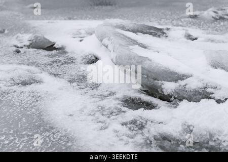 High contrast monochrome image showing textures of frozen water and snow on a sandy shoreline. Large chunks of ice are scattered across the coast. Stock Photo