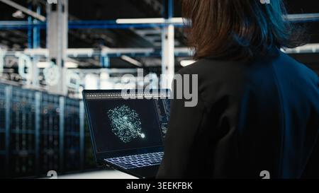 Data center female programmer using AI LLM model on laptop to optimize equipment rigs. Woman in server hub using large language model neural network technology to adjust system parameters Stock Photo