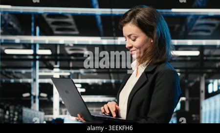 Smiling data center female engineer pleased after upgrading AI systems. Happy server room manager proud after successful artificial intelligence deployment with VFX holographic data overlay Stock Photo