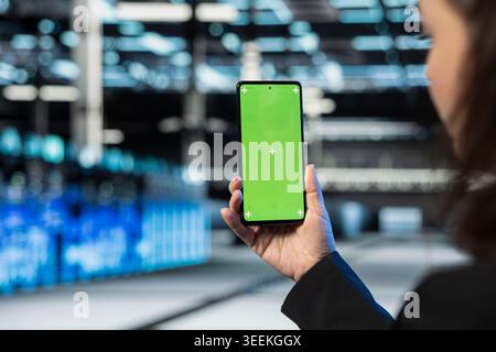 Green screen smartphone used by server farm technician looking over maintenance diagnostic reports to optimize gear performance. Data center employee reading system technical files on mockup phone Stock Photo