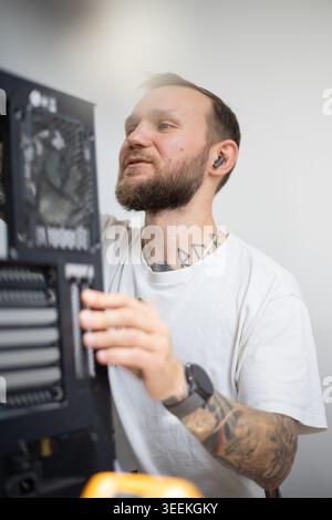 Man building computer case in workshop while wearing casual clothes and listening to music Stock Photo