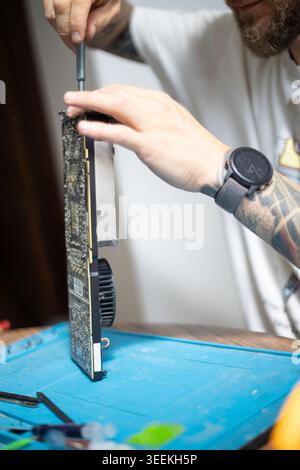 Person repairs a computer graphics card on a table in a home setting during the day Stock Photo