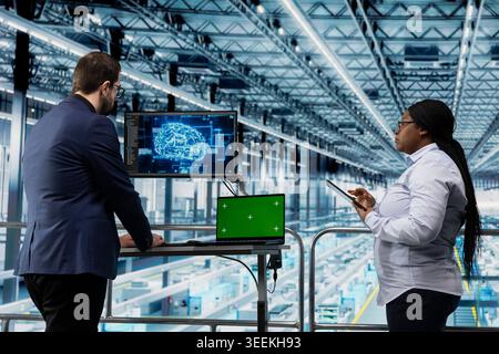 Green screen mockup laptop in microchip factory and AI used by workers to visualize machinery data. Employees using chroma key isolated screen notebook and deep learning in manufacturing plant Stock Photo