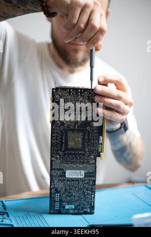 Person works on computer hardware in a bright room while holding a screwdriver in their hand and focusing on the task Stock Photo