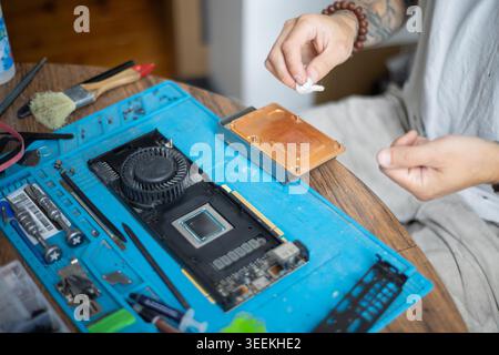 Person repairs a computer graphics card on a blue workbench in a well-lit indoor space during the day Stock Photo