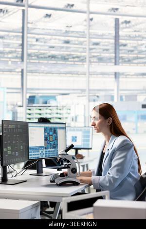 Female technician observing microchip layout with microscope in RD office. Engineer doing innovative study using microscopy tool, researching materials for nanotechnology development Stock Photo