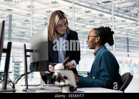African american woman and manager observing microchip layout with microscope in RD office. Teamworking colleagues doing innovative study using microscopy tool, researching materials Stock Photo