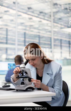 Examining PCB circuitry, microscope and researcher analyzing hardware components. Evaluating electronic prototypes, optical instrument and technician in semiconductor manufacturing plant RD office Stock Photo