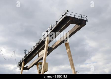 Large, heavy-duty industrial overhead crane. Its prominent steel beams, supportive beige legs, operator control cabin, and service walkways are set ag Stock Photo