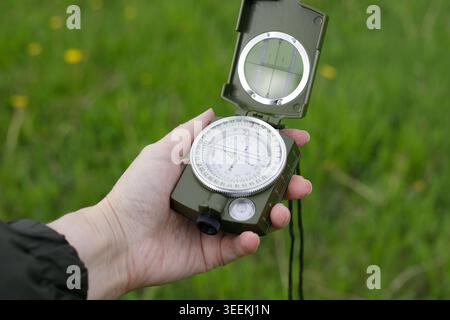 Woman's hand holding a opened compass for orientation against a background of green grass. Travel and navigation concept. Space for text. Stock Photo