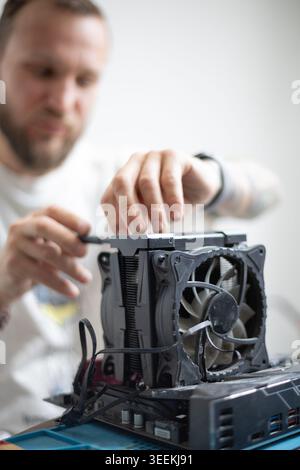 Man works on assembling a computer component in a bright room with a focus on the cooling fan setup and personal effort involved in the task Stock Photo