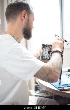 Man works on computer fan at home desk while adjusting tool in bright setting during daytime Stock Photo
