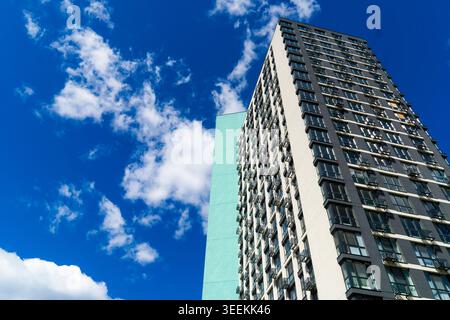 Low angle view of modern high rise apartment building tower with stylish facade against vibrant blue sky with fluffy white clouds Stock Photo