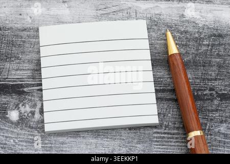 A top down view of a white lined notepad and elegant wooden pen on a weathered gray timber surface. Stock Photo