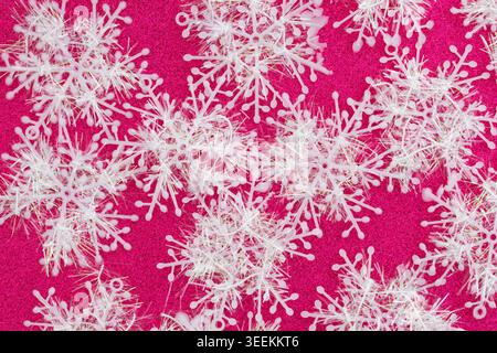 White decorative snowflakes scattered on bright pink glitter background, creating a festive winter holiday texture for Christmas designs and seasonal Stock Photo