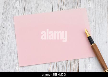 Soft pink blank card mockup with fountain pen on white wood desk, ideal for branding, invitation, stationery, and message design Stock Photo