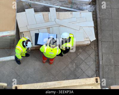 Three workers in high visibility jackets discuss documents at construction site together Stock Photo