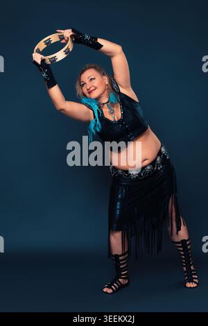 Smiling female performer engages in captivating percussive dance, her movements accompanied by rhythmic striking of tambourine. Caucasian female dance Stock Photo