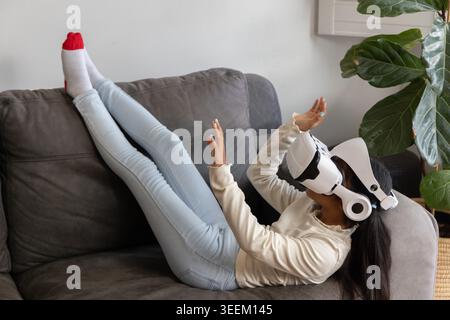 African American child reclining on living room gray sofa wearing VR headset and red-toed socks Stock Photo