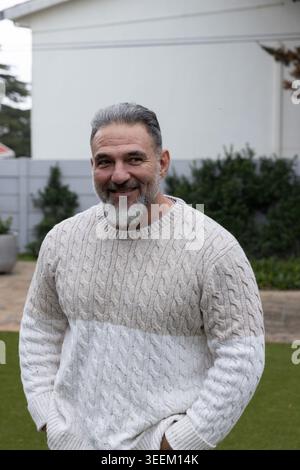 Senior man standing on green lawn in front of house wearing two-tone cable-knit sweater Stock Photo