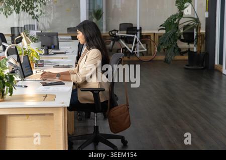 Female worker starting typing on laptop at open office, causing animated charts showing tasks Stock Photo
