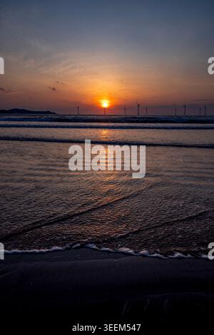sunset over beach with offshore wind turbines Stock Photo