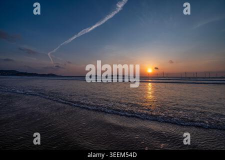 sunset over beach with offshore wind turbines Stock Photo