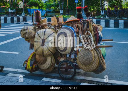 Wooden street vendor cart displaying various handcrafted bamboo baskets, winnowing trays, and traditional household tools on an urban roadside. Stock Photo