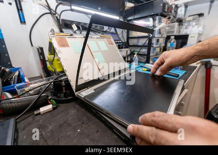 Professional technician repairing a laptop computer on a cluttered workbench in a technical service center, Queensland, Australia. (2025) Stock Photo