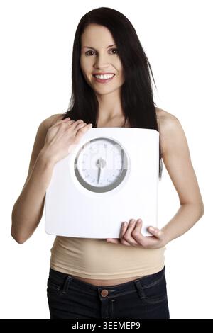 Happy young beautiful woman is standing and smiling and showing white weight. Casual dress and long hair. Isolated on the white background Stock Photo