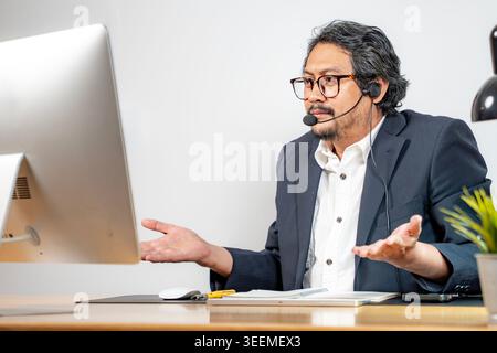 A young male professional communicates with colleagues through a virtual meeting on his laptop in a modern office setting. Stock Photo