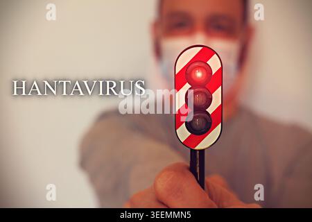 Person wearing protective face mask standing beside a red traffic light with Hantavirus text, conceptual image about virus outbreak, public health war Stock Photo
