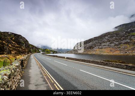 A scenic landscape photograph looking down the historic A5 trunk road as it curves alongside the shores of Llyn Ogwen in North Wales. To the right, th Stock Photo