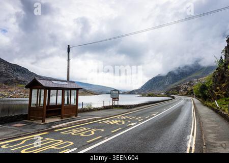 Wide-angle landscape featuring a traditional wooden bus shelter situated on the A5 road overlooking Llyn Ogwen in North Wales.  The road markings Safl Stock Photo