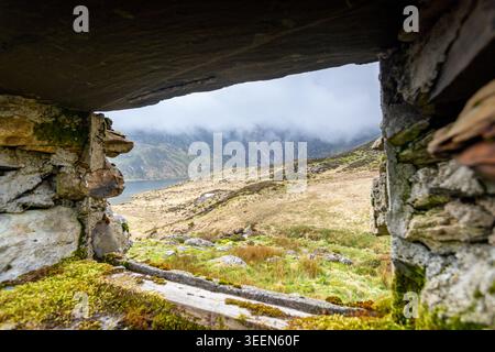 An evocative landscape looking through a narrow, weathered stone aperture toward Llyn Idwal in the Ogwen Valley.  The foreground features the rough, m Stock Photo