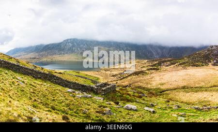 A wide panorama overlooking the dramatic bowl of Cwm Idwal in North Wales. In the foreground, a traditional Welsh dry stone wall and a small, rectangu Stock Photo